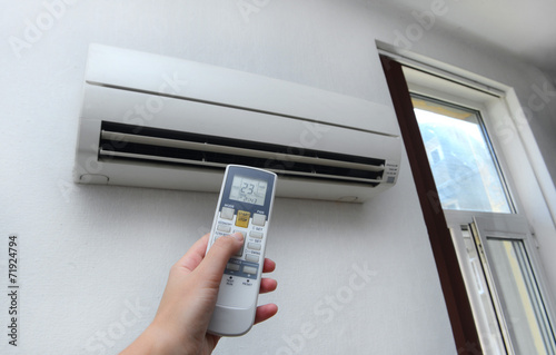 Hand with remote control directed on the conditioner on the wall