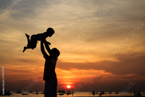 father and son silhouettes play at the beach