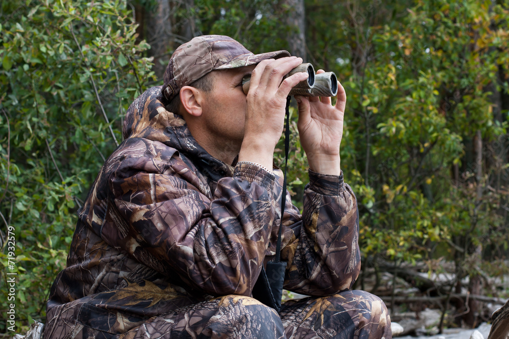 sitting hunter  looks through the binoculars