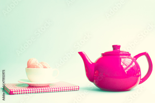 Pink macaroons in a white tea cup over book and red teapot