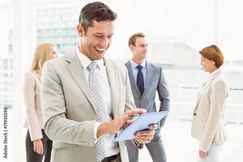 Businessman using digital tablet with colleagues behind Businessman using digital tablet with colleagues behind