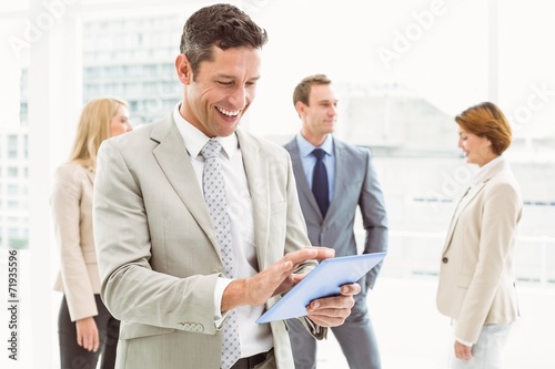 Businessman using digital tablet with colleagues behind