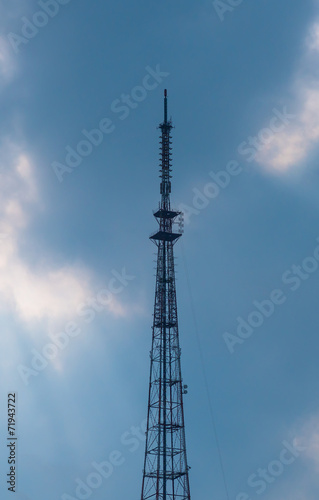 Telecommunications tower on the background of cloudy sky.