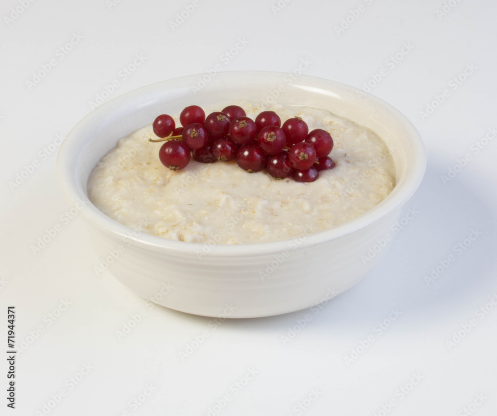 Bowl of oats porridge with red currant  on a white background