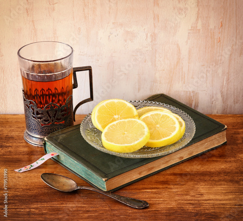 vintage tea glass-holder with fresh lemons and old book over woo
