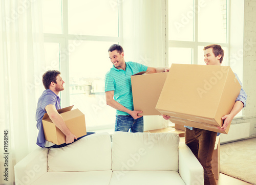 smiling male friends carrying boxes at new place