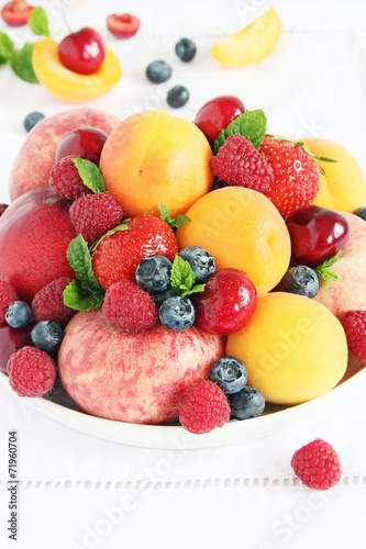 Plate with seasonal fruits and berries on white background.