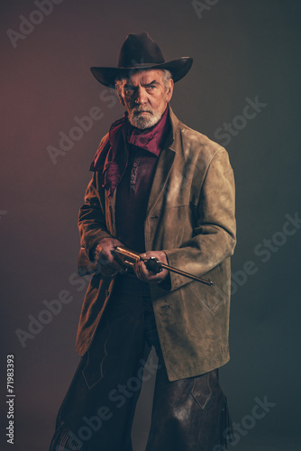 Old rough western cowboy with gray beard and brown hat holding r photo