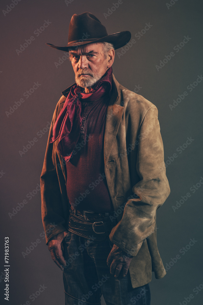 Old rough western cowboy with gray beard and brown hat. Low key