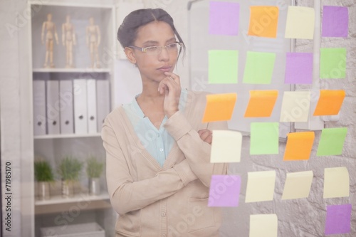 Thoughtful businesswoman looking at sticky notes on window