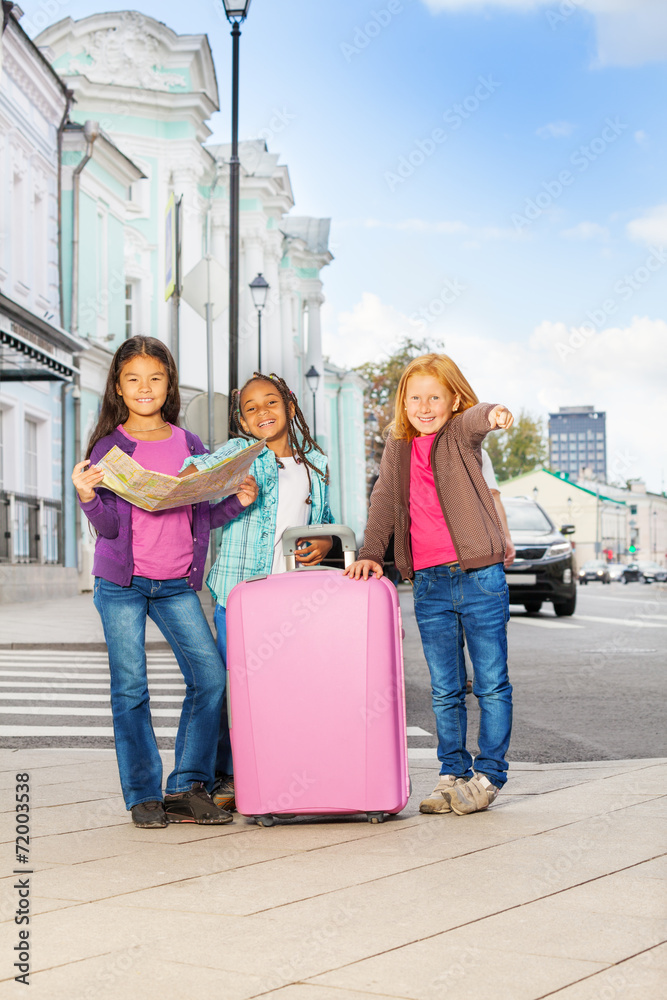 Three smiling girls stand with map and luggage