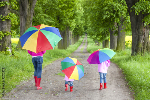 mother and her daughters with umbrellas in spring alley