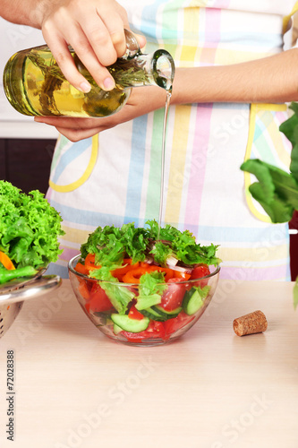 Woman pouring olive oil in vegetable salad in kitchen