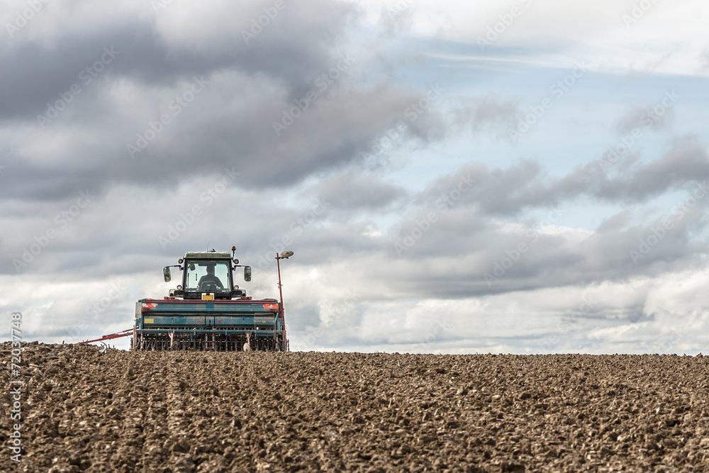 tractor seeding in a field on cloudy sky background tractor seeding in a field on cloudy sky background