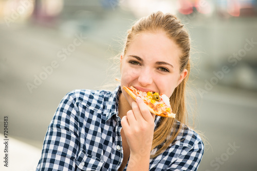 Teenager eating pizza in street