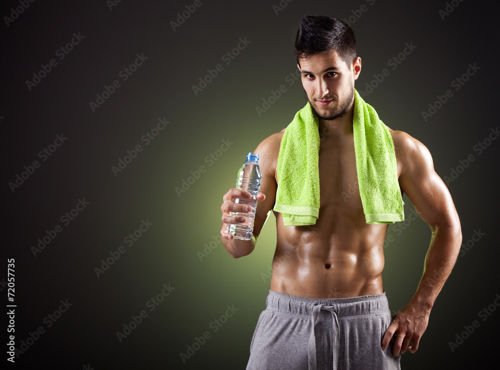 Fitness man holding a bottle of fresh water on dark background