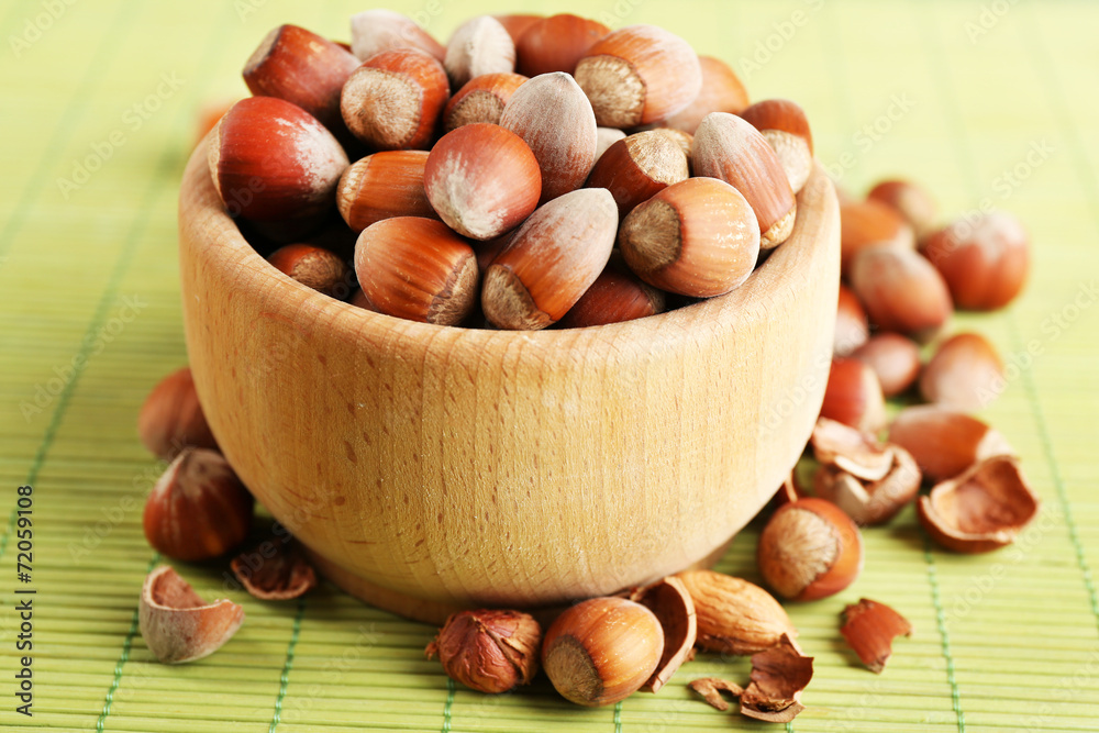 Hazelnuts in wooden bowl on bamboo mat background Hazelnuts in wooden bowl on bamboo mat background