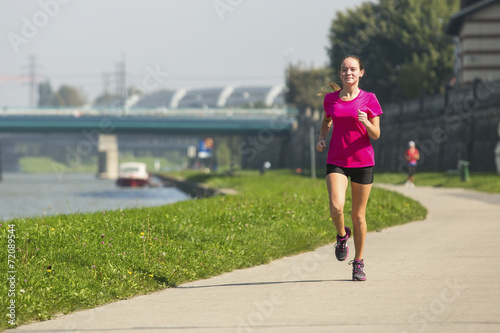 Young girl jogging near the river embankment.
