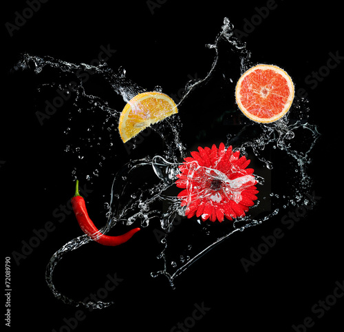 Fresh fruits and flowers in water splash, on black background
