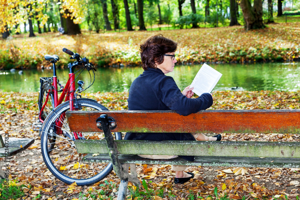 Woman with bicycle sitting in the park and reads
