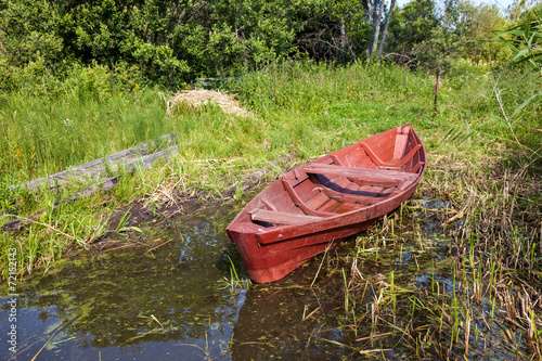Old fishing wooden boat at the bank of lake in summer day
