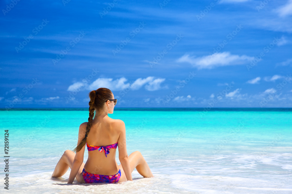 Beautiful young woman in bikini sitting on tropical beach