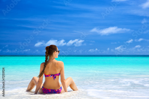 Beautiful young woman in bikini sitting on tropical beach © Oleksandr Dibrova