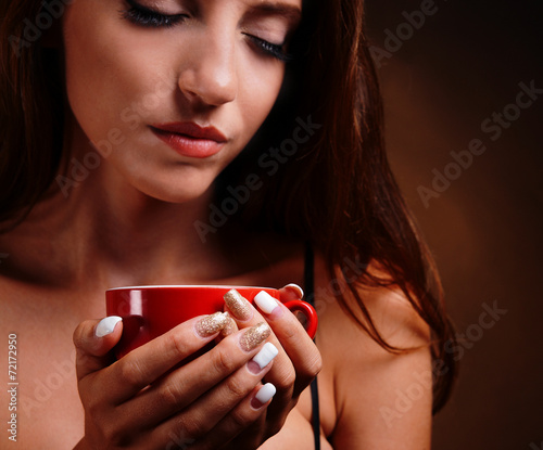 Beautiful young girl with cup of coffee on brown background