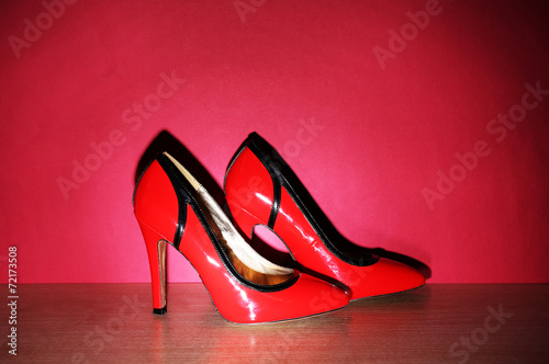 Pair of woman's red shoes on floor on red wall background