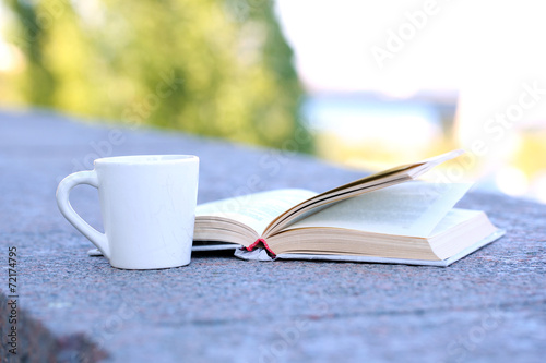 Cup with hot drink and book, outdoors