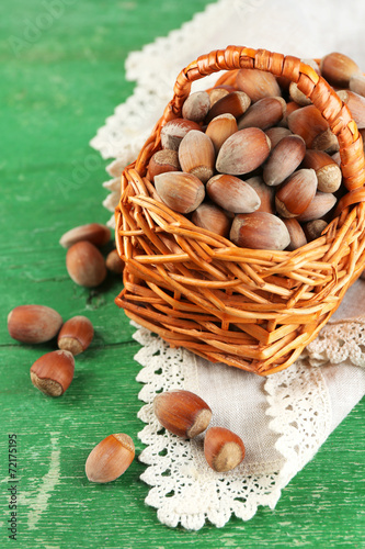 Hazelnuts in wicker basket, on napkin on wooden background