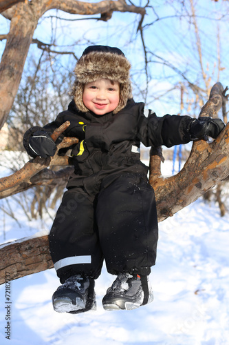 happy 2 year toddler sitting on tree in winter