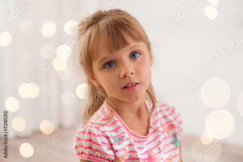 Cute little girl at home. Holiday lights around. © tananddda