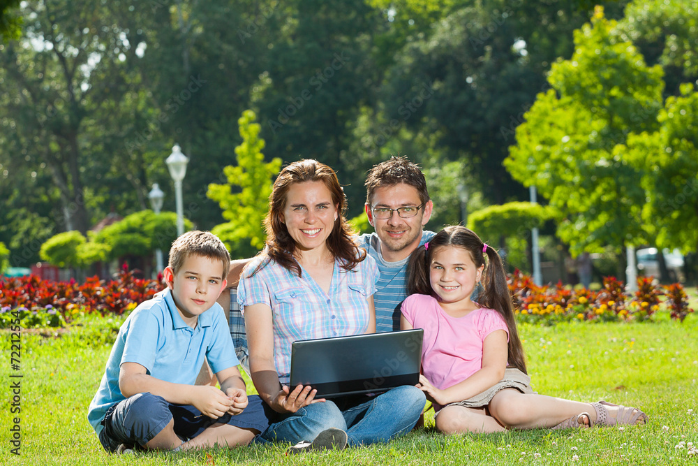 Happy Family using laptop lying on grass Happy Family using laptop lying on grass