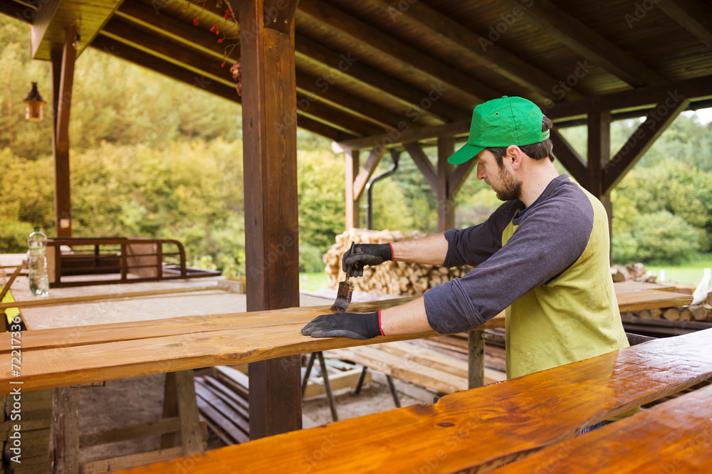 Handyman varnishing wooden planks outside
