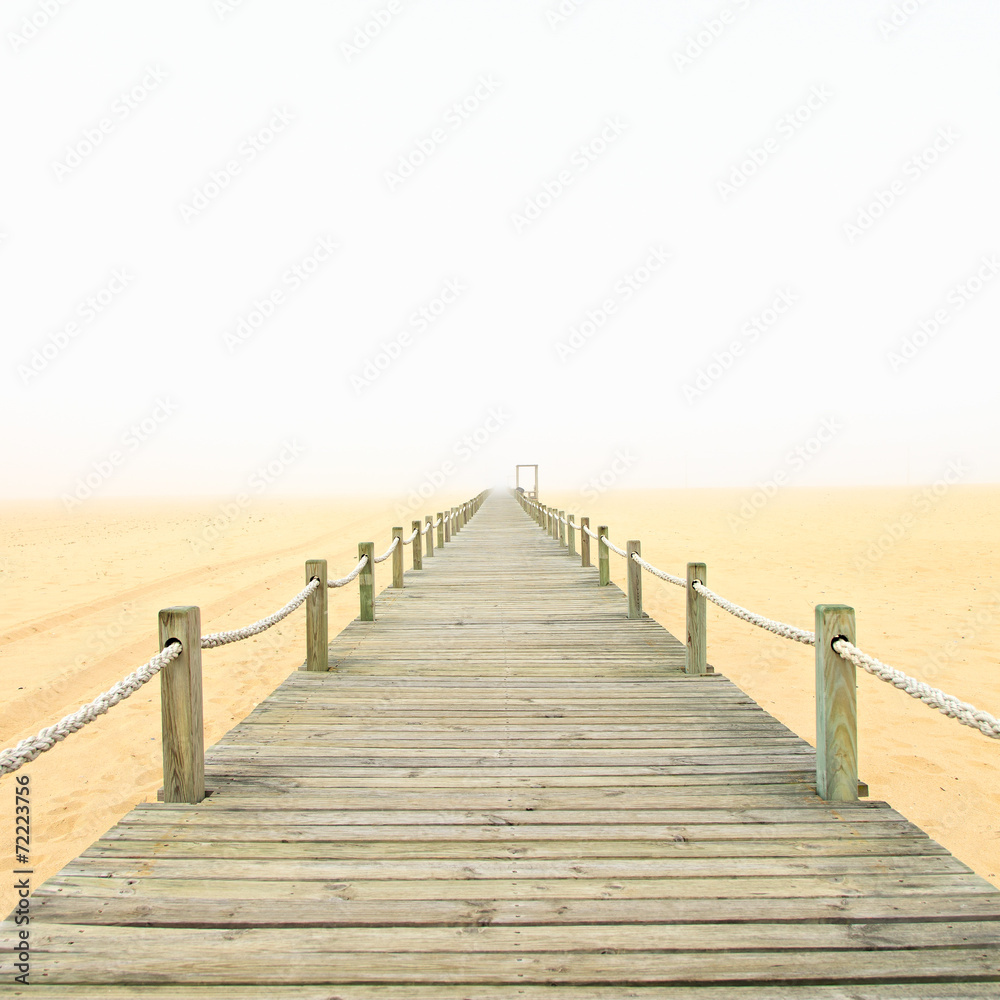 Fototapeta premium Wooden footbridge on a foggy sand beach background. Portugal.