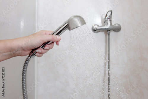 Womens hand holding shower head with pouring water in domestic