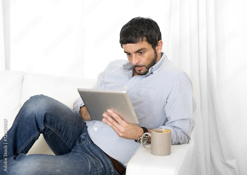 Hispanic man on couch working with digital tablet or pad