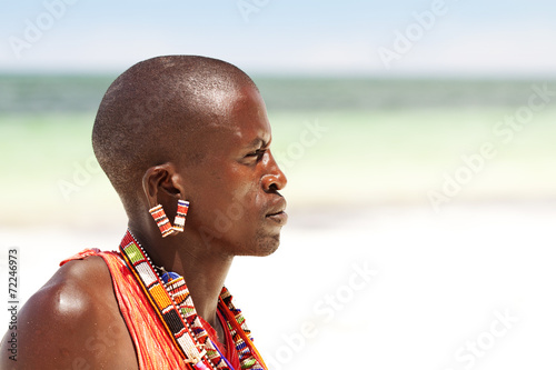 Young massai warrior man posing on bright sunny beach in Kenya photo