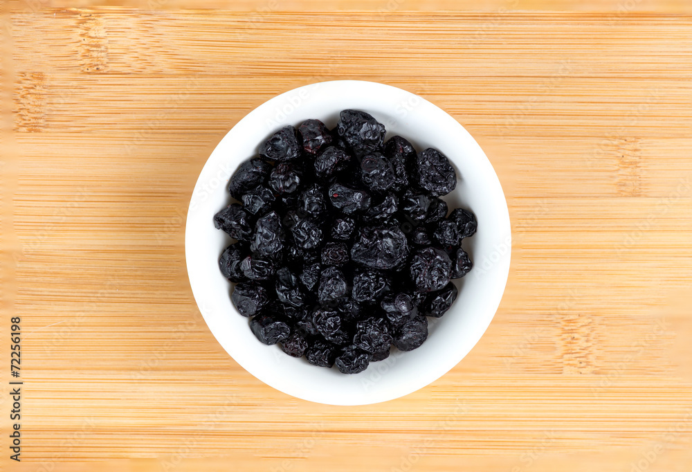 Dehydrated blueberries in bowl against wooden board Dehydrated blueberries in bowl against wooden board