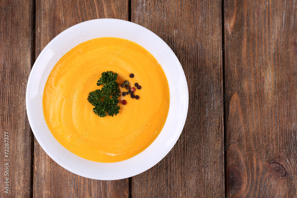 Pumpkin soup in white plate on wooden background Pumpkin soup in white plate on wooden background