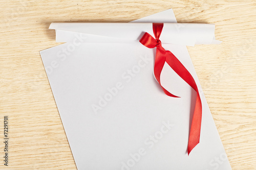 Scroll of paper with a red ribbon on a wooden surface.