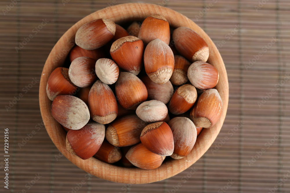 Hazelnuts in wooden bowl on bamboo mat background