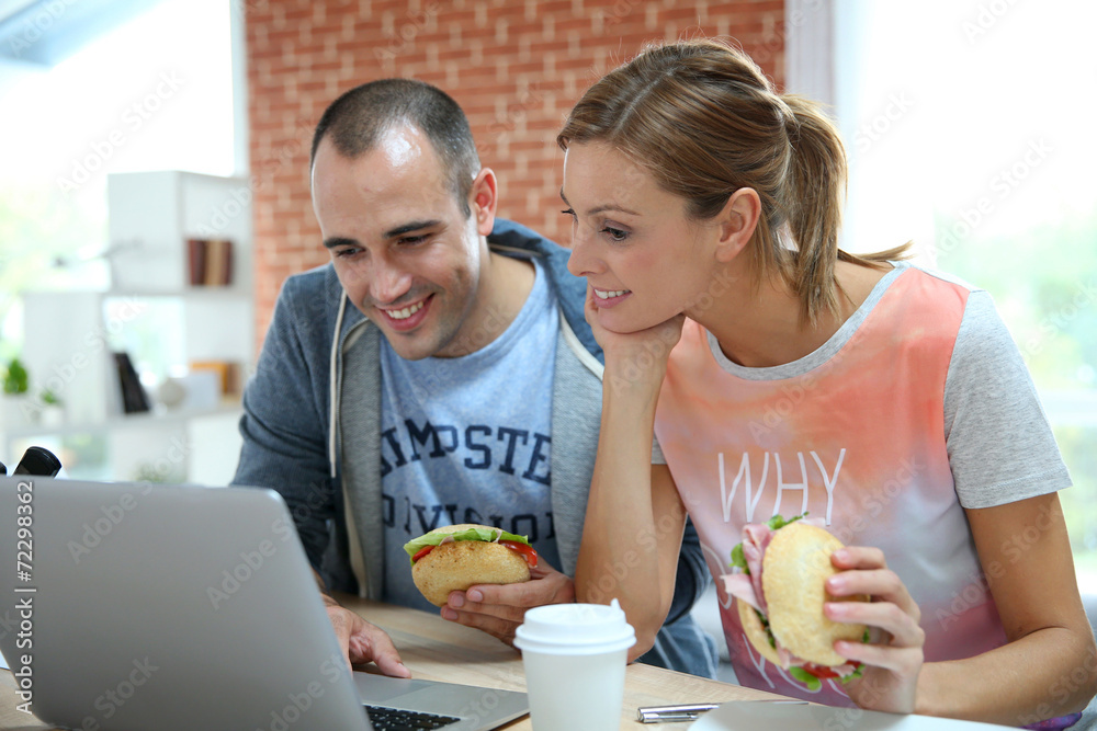 Roommates eating sandwich in front of laptop Roommates eating sandwich in front of laptop