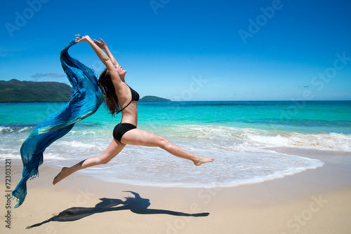 Young girl jumping with waving blue scarf tropical beach
