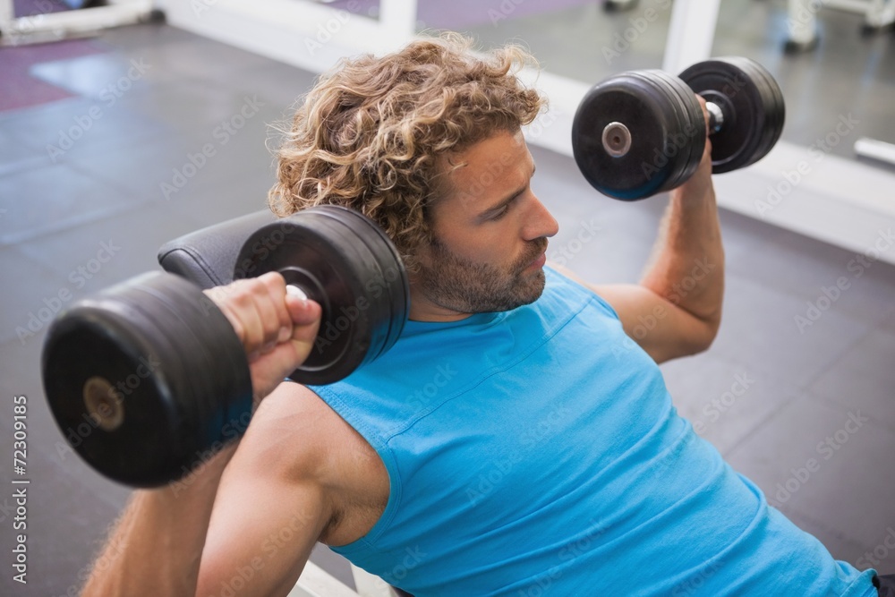 Side view of man exercising with dumbbells in gym