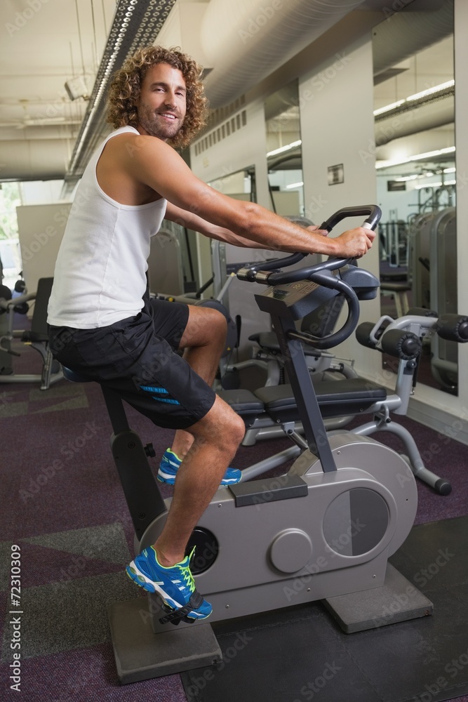 Fototapeta premium Side view of man working out on exercise bike at gym