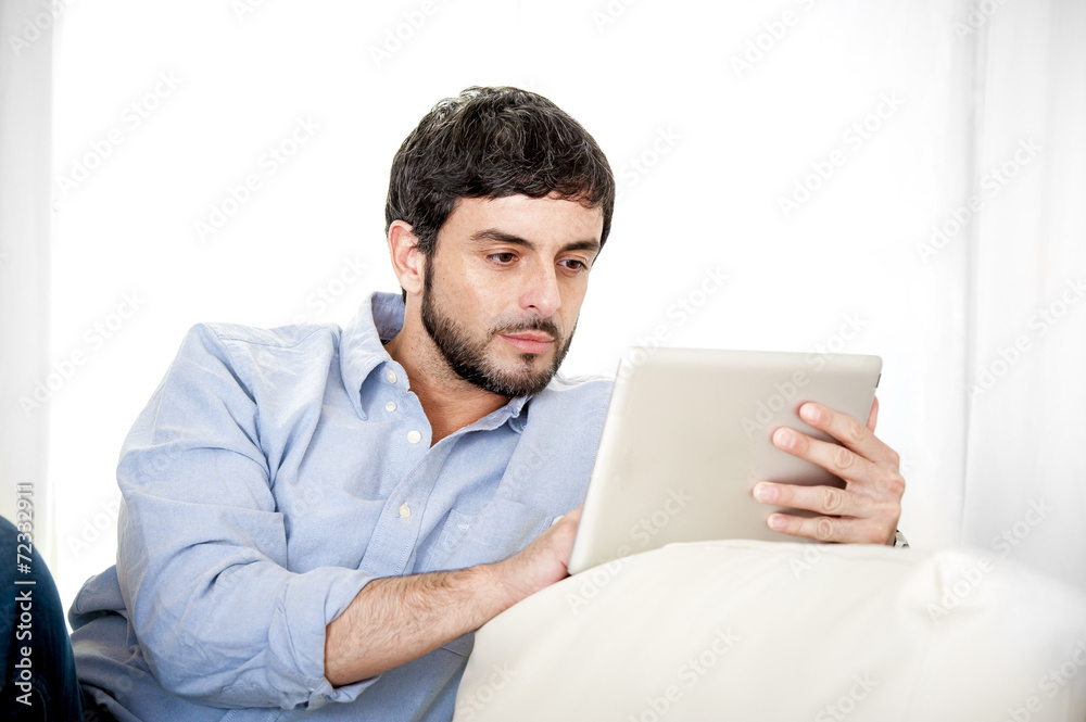 Young attractive Hispanic man at home using digital tablet pad