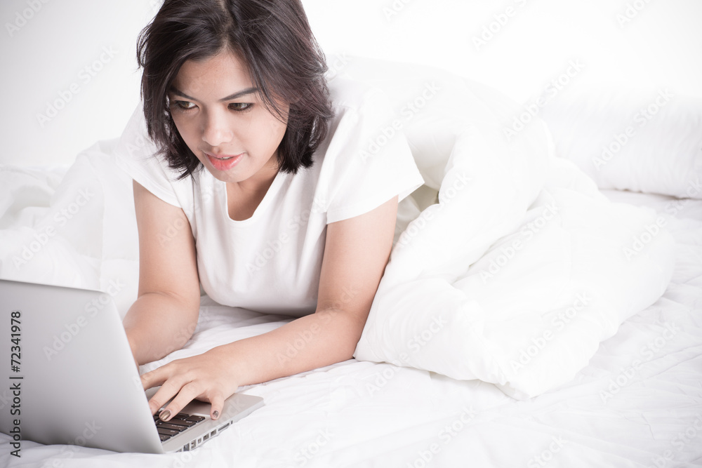 Smiling woman using a laptop while lying on her bed Smiling woman using a laptop while lying on her bed