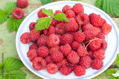 Fresh raspberries on a plate on old wooden table.